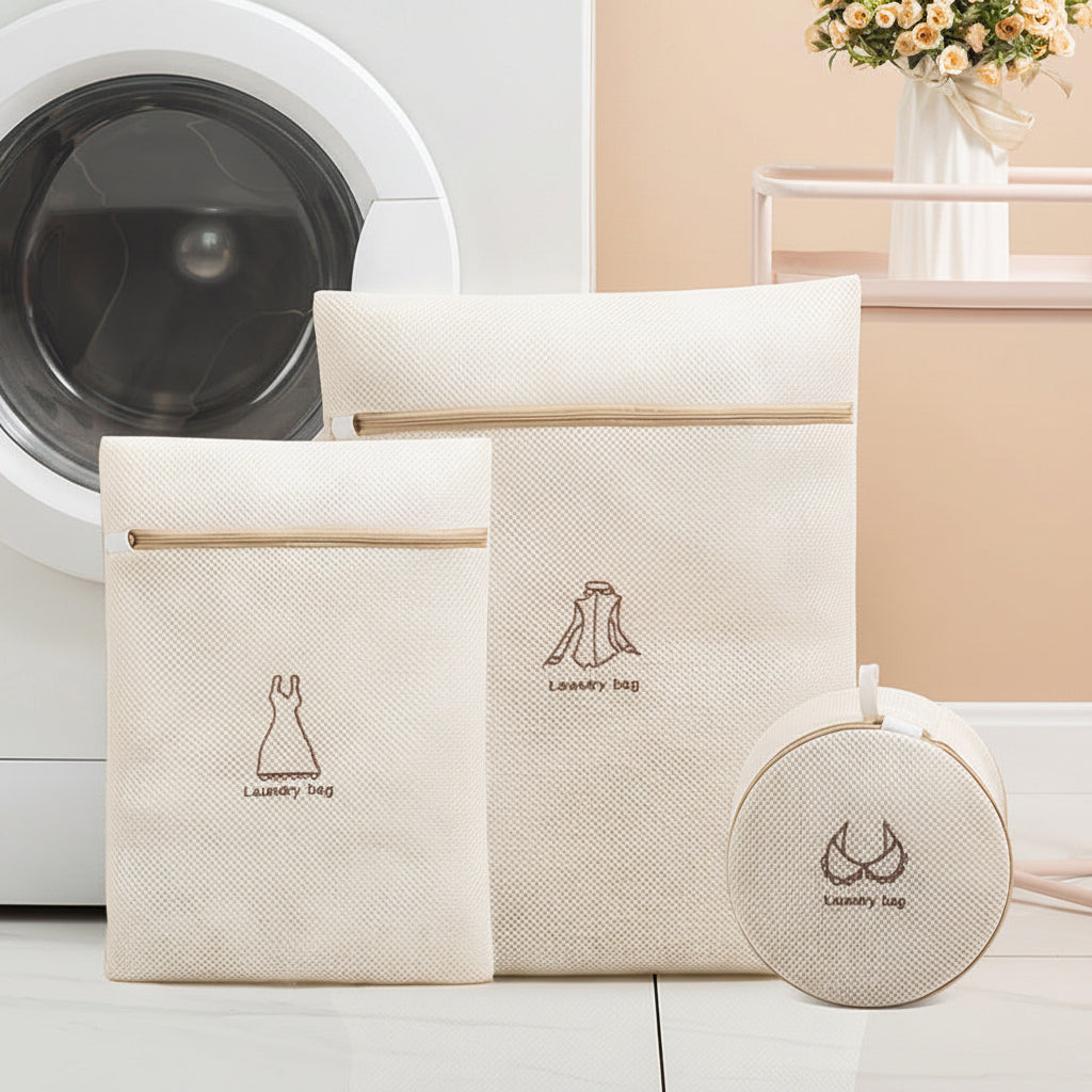 Set of beige laundry bags with logo in front of a washing machine.