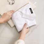 White shirt with a tag on a beige surface, held by hands.